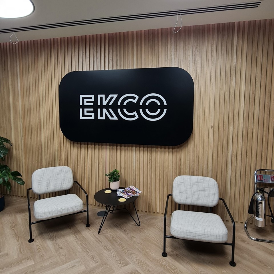 An illuminated black and white reception sign which reads ECKO with two chairs below it